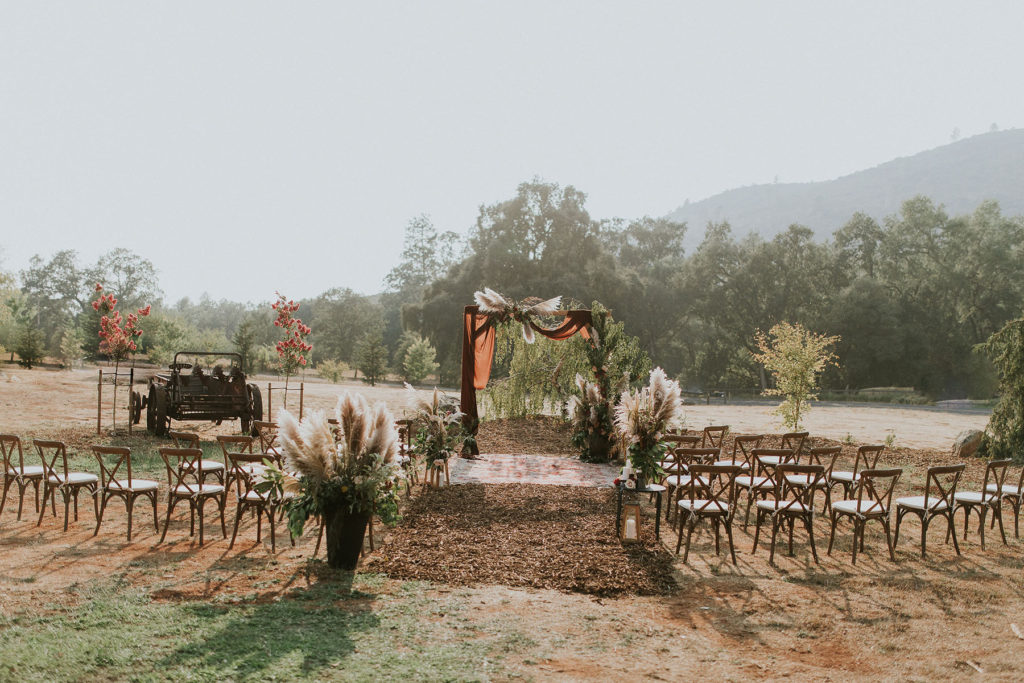 Photo of cross back chairs with cushions at rustic outdoor wedding ceremony site.