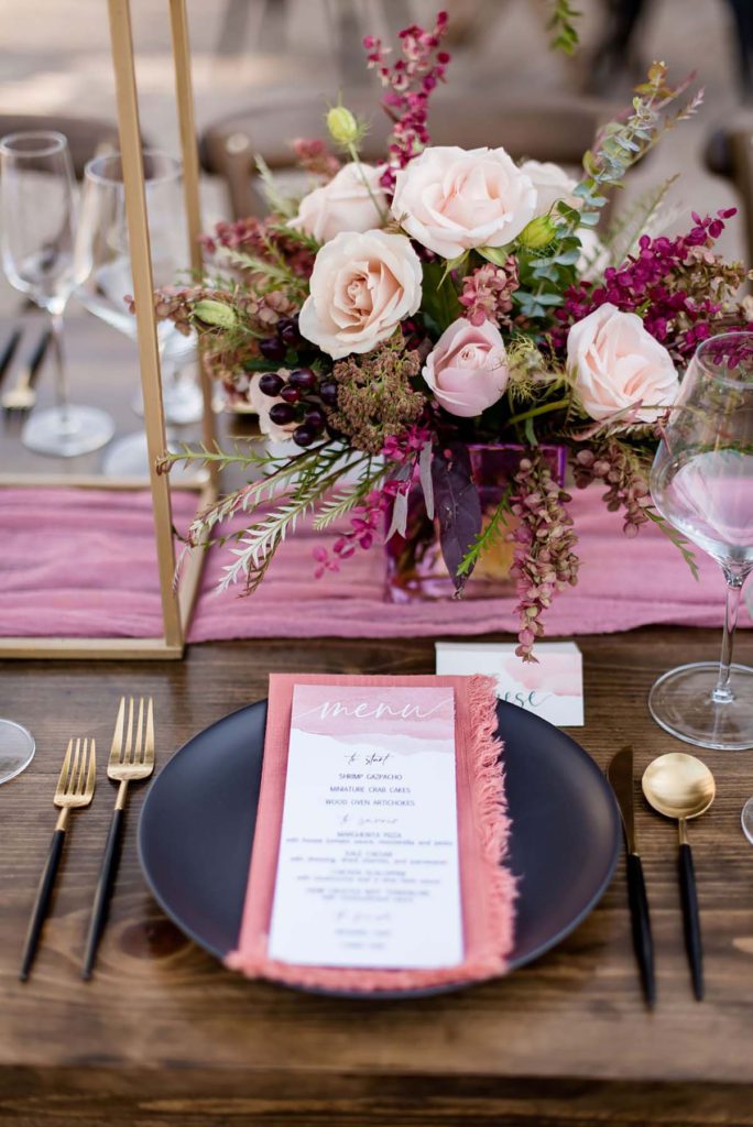 Table setting with flowers, matte black plates, flowers and clear glassware.