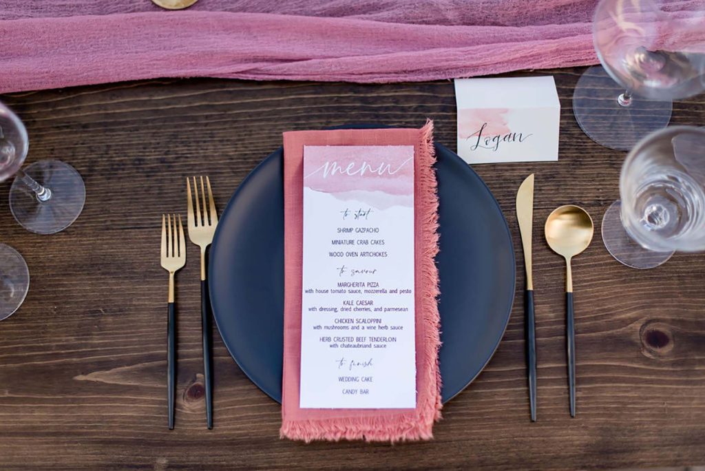 Place setting with menu, matte black plate and gold flatware.